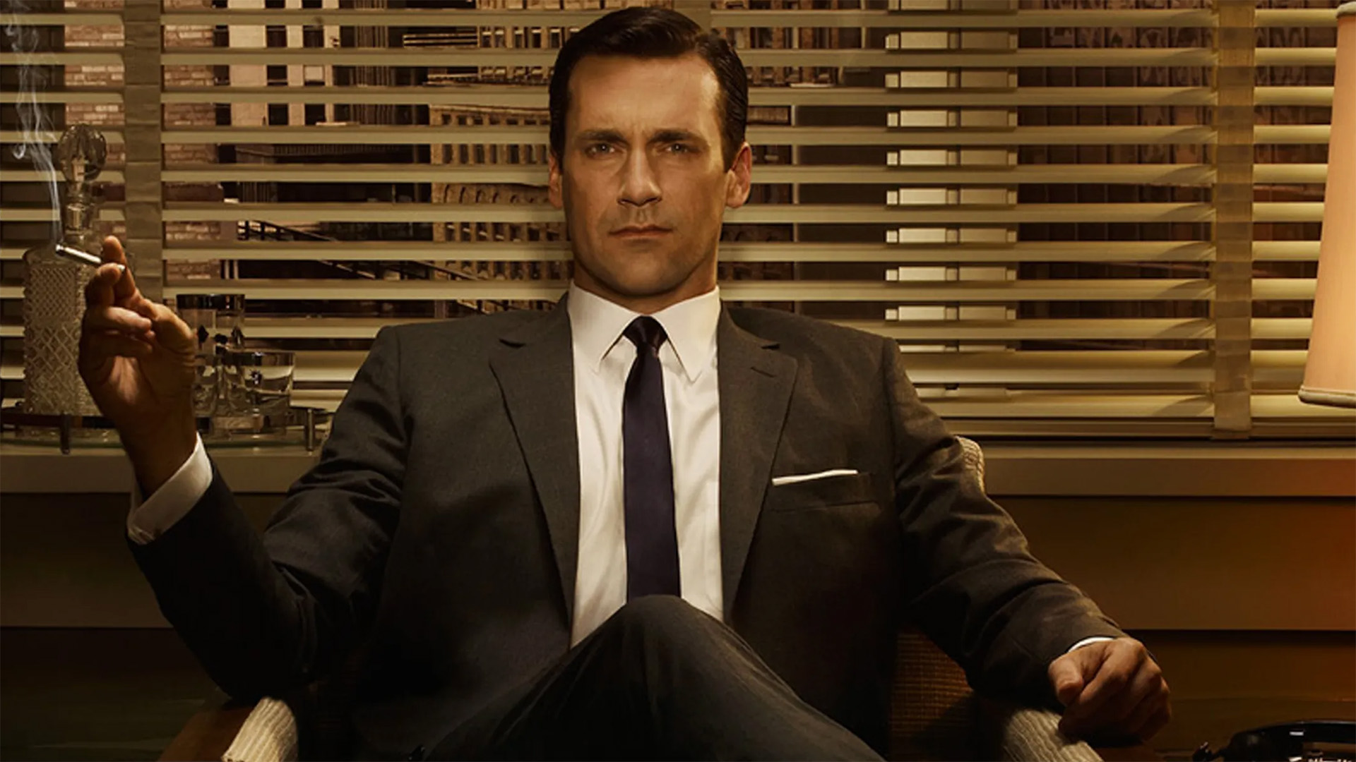 Jon Hamm as Don Draper in Mad Men, smoking a cigarette in a chair.